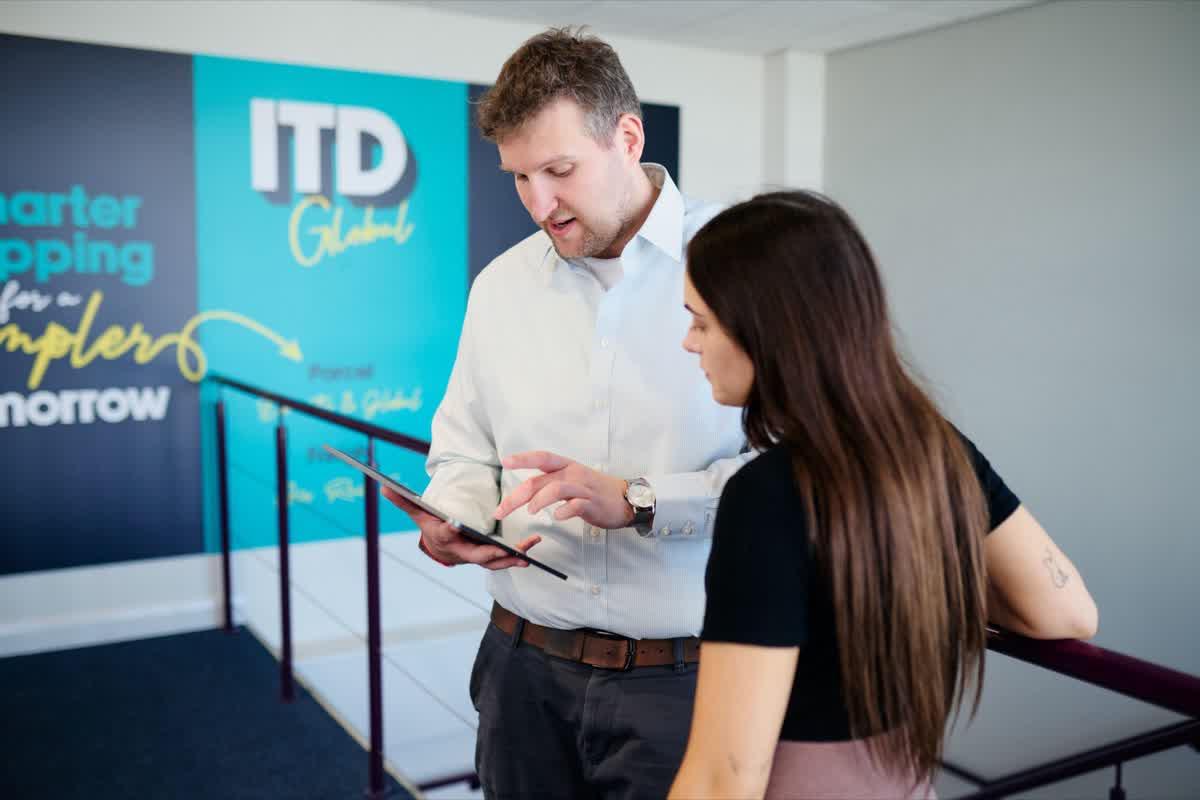 ITD Global colleagues reviewing a tablet by the company mural