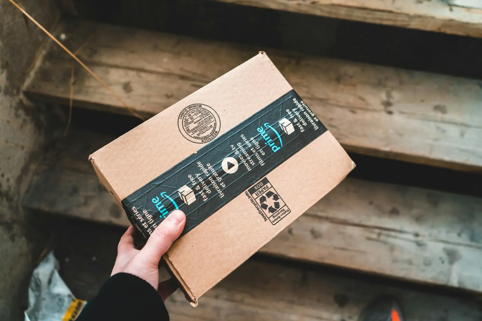 Hand holding an Amazon Prime parcel on UK doorstep steps