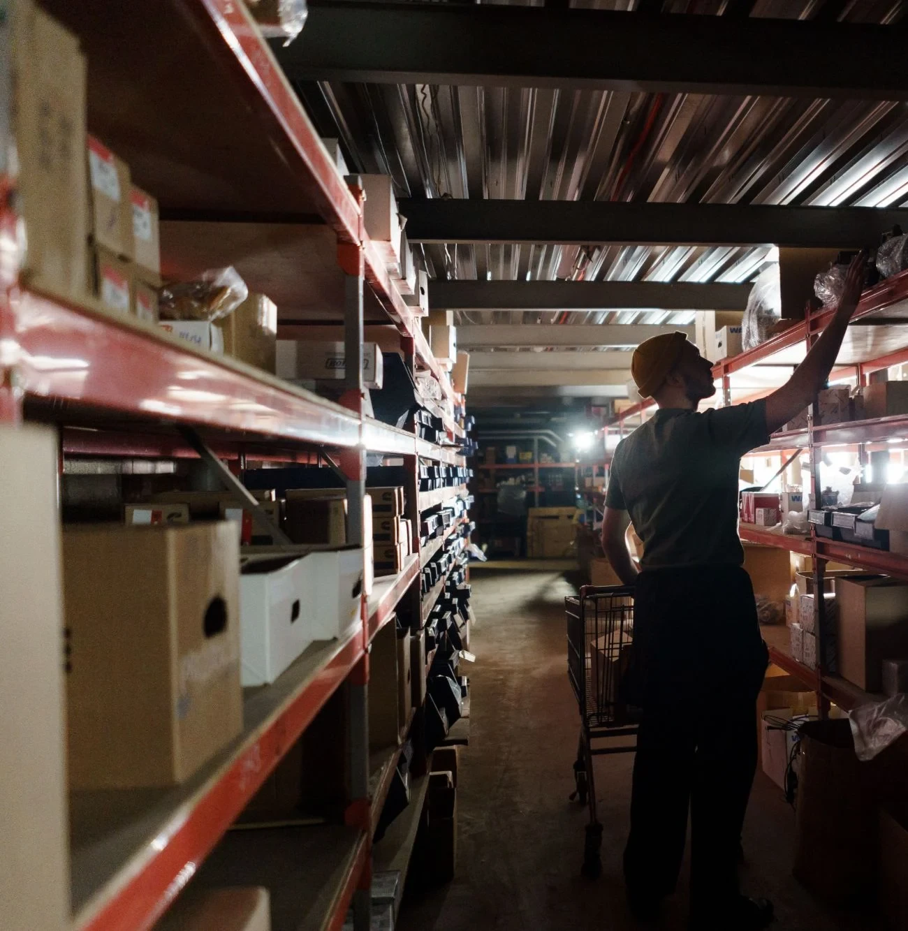 Warehouse operative with a picking trolley reaching stock from racking in a 3PL fulfilment centre